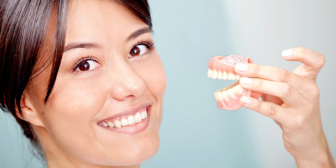 пациентка с макетом челюсти для подготовки к протезированию зубов у стоматолога хирурга