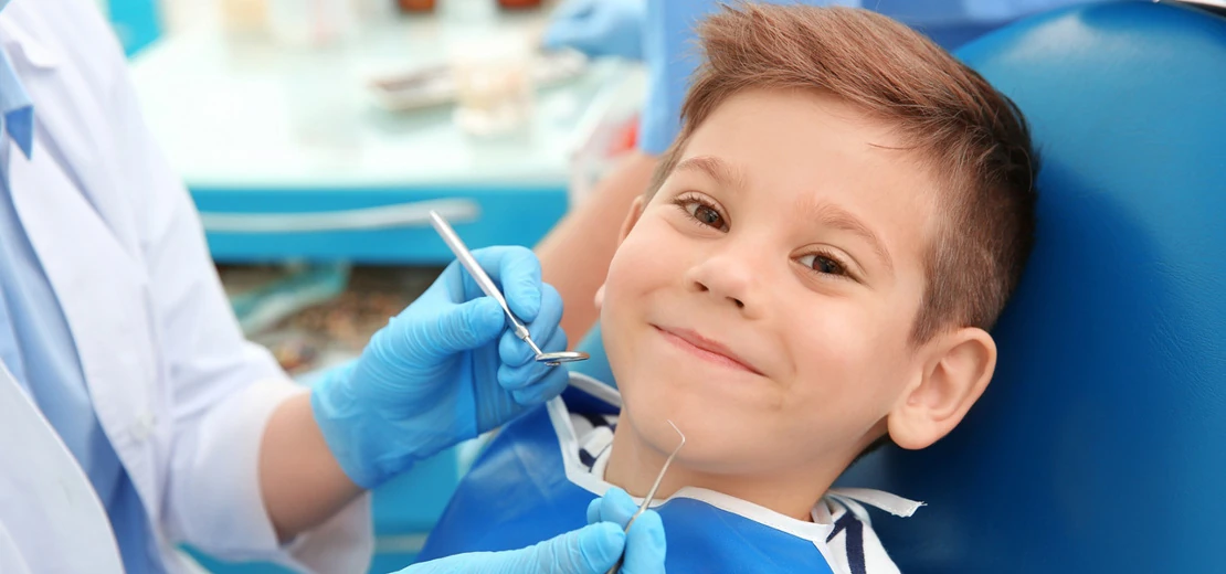 на фото малыш в отделении Детская стоматология лечит зубы, сидя в кресле
